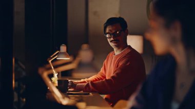 Karanlık çalışma alanındaki geç dönem çalışanları takım çalışmasının keyfini çıkarıyorlar. Profesyonel kadın yönetici, gece ofisindeki iş arkadaşına gülümsüyor. Serbest çalışanlar lamba ışığında birlikte çalışıyorlar. Profesyonel işbirliği..