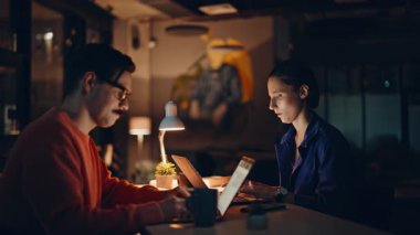 Gece iş yerinde dizüstü bilgisayar arayan çok çalışan yöneticiler. Gergin takım arkadaşları lamba ışığında birlikte çalışıyorlar. İki çalışanın ofiste geç saatlere kadar çalışmaktan yorulması..