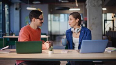 Rahatlamış ekip üyeleri laptopun iş yerinde kahve içiyorlar. Yakın plan. Dost canlısı iş adamları modern çalışma alanlarında oturarak tatil yapıyorlar. İki meslektaş kafeteryada içki yudumlarken konuşuyor..