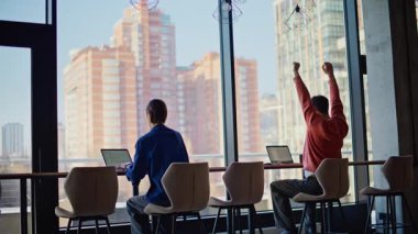 Çevrimiçi yöneticiler modern ofis ortamında işbirliği yapıyorlar. Panoramik pencere eşzamanlı çalışma alanında dizüstü bilgisayarda çalışan iki profesyonel çalışan. Gözlüklü adam elini uzatıyor ve meşgul iş kadınıyla konuşuyor..