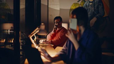 Çevrimiçi yöneticiler karanlık şirket ofisindeki müşterileri arıyor. Arkadaş canlısı bir kadın iş yerinde iş arkadaşına gülümseyen bir cep telefonuyla konuşuyor. İki iş danışmanı fazla mesai yapıyor..