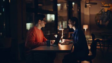 Mesai arkadaşları gece ofislerinde iletişim kuruyor. Gülümseyen bıyıklı adam dizüstü bilgisayarlarda çalışan bir kadınla konuşuyor. Gece geç saatlerde bilgisayarları daktilo eden iki uzman..