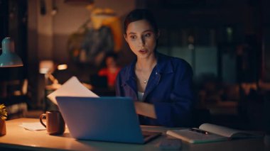 İş kadını, gece iş yerindeki yakın çekim sırasında video ile kağıtları tartışıyor. Endişeli kadın yöneticinin dizüstü bilgisayarı kapatması stresli bir konuşmaydı. Çevrimiçi sohbetteki raporlardaki hatadan şikayetçi.