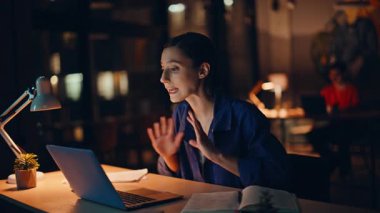 Sinirli iş kadını, dizüstü bilgisayarda web kamerasına el kol hareketi yapıyor. Gece ofis kapanışında fazla mesai yapıyor. Endişeli kadın görüntülü arama ile tartışıyor. Gergin muhasebeci online sohbette belgeden şikayetçi.