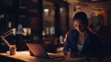 Gece çalışan odaklı iş kadını Dark Company 'nin iç çekimlerinde dizüstü bilgisayara bakıyor. Profesyonel yönetici, not yazma sitesi. Çalışkan kadın girişimci fazla mesai projesi geliştiriyor.