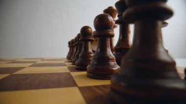 Kahverengi ahşap satranç taşları yakın planda. Sıraya dizilmiş karanlık figürler. Çözümlemeye başlayan taktikleri temsil eden tek kişilik oyun detaylarına vurgu yapılmıştır. Oyun senaryosunda sakin ol