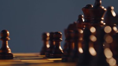 Kara satranç figürleri tahtaya yakın planda. Kareli kareler boyunca akan güneş ışığı gölgeler oluşturur. İki piyon parçası taktiksel bir fırsat olduğunu gösteriyor. Zihinsel savaş başlatılıyor.