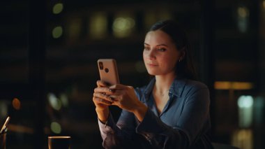 Geceleri şirketlerin iş yerinde cep telefonuyla konuşan sırıtan esmer. Akıllı telefondan sosyal medyayı izleyen neşeli iş kadını karanlık ofiste oturuyor. İnternetten alışveriş yapan rahat kadın..