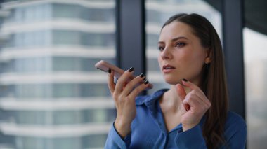 Ofisteki cep telefonu hoparlöründen konuşan çalışanların sesli mesajlarını kaydediyorum. Zarif iş kadını pencerenin yanındaki akıllı telefonda sesli mesaj bırakmış. Hoparlörden konuşan kendinden emin bir kadın..