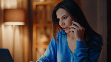 Akşam oturma odasında oturan bir kadın dizüstü bilgisayarları internetten kontrol ediyor. Kendine güvenen iş kadını cep telefonu görünümlü bilgisayar konuşuyor. Gülümseyen bayan müdür geç saatte telefonla danışmanlık yapıyor.