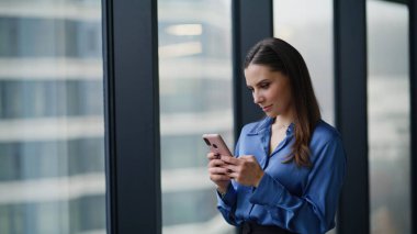 Gülümseyen girişimci cep telefonu mesajlaşması ofis salonunu kapatıyor. Rahatlamış iş kadını panoramik pencereden akıllı telefona mesaj atıyor. Zarif kadın CEO cep telefonunda SMS okuyor sosyal medyada geziniyor.