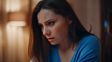Sorunlu kadın akşam evde oturup sorunlarını yakından düşünüyor. Stresli esmer, başını tutuyor. Karanlık dairede duygusal gerginlik yaşıyor. Endişeli kadın lamba ışığı altında kaygılanıyor..