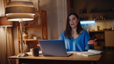 Sanal konferansta çalışan danışman gece evde dizüstü bilgisayara el kol hareketi yapıyor. Gülümseyen kadın serbest çalışan video ile görevi açıklıyor. Neşeli esmer, akşam saatlerinde internette konuşuyor.