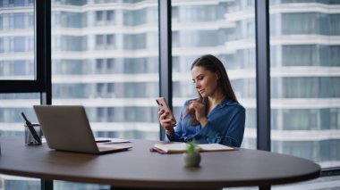 Ofis çalışanı akıllı telefondan sosyal medyayı izliyor. Ofiste mola veriyor. İş yerinde cep telefonu mesajı okurken gülümseyen zarif bir esmer. Başarılı kadın yönetici çevrimiçi telefon iletişiminden hoşlanıyor.
