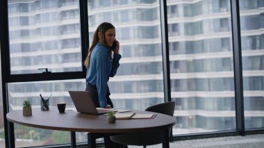 Yönetici, ofis masasına yaslanarak akıllı telefon pazarlığı yapıyor. Lüks iş yerinde panoramik pencereli cep telefonuyla konuşan zarif bir iş kadını. Başarılı kadın patron arıyor..