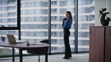 Düşünceli iş kadını elinde cep telefonuyla panoramik pencereye bakıyor. Modern ofis işini düşünen zarif bir kadın CEO. Şirketin iş yerinde sakin, esmer görünümlü akıllı telefon..