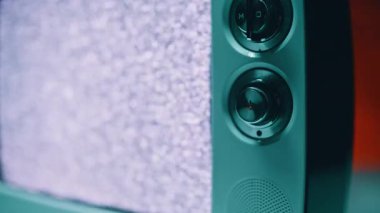 Eski tarz televizyon yakından bakınca titreşen parazitleri gösteriyor. Parmak dokunuşu paneli antika cihazın kadranını döndürüyor. Kırık sinyal cam ekranda yanıp sönen çizgilere ve gürültü kalıplarına neden olur. 