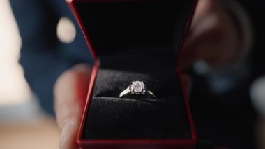 Erkek eller özel olarak aşk hediyesini sunar. Yakın çekim görüntüsünü ayarlar. Özel evlenme teklif sahnesi hazırlayan meçhul romantik kişi. Gizli figür, parlak yaşam alanındaki kadife kutudan zarif bir halka ortaya çıkarır