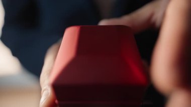 Erkek parmakları kapalı mekanda nişan teklifi yapıyor. Anonim aşık adam eşsiz bir romantik an yaratıyor. Tanımlanamayan beyefendi kırmızı kutuyu açıyor. Işıklı dairede tek başına parlak bir yüzük gösteriyor.