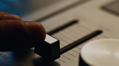 Müzisyen eli, karanlık odada klasik stereo konsolda ses dengesini ayarlıyor. Kaypak levrek ölçeğinde nazikçe hareket eder ve titizlikle üç katına çıkar. İçerideki bilinmeyen ses teknisyeni ayarlama paneli.