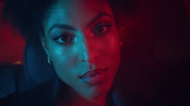 Parlak makyajlı, yakın plan kadın yüzü kırmızı neon ışığı yaktı. Güzel bir afro-amerikan bayanın portresi siyah bir arabada tek başına oturuyor. Gece poz veren muhteşem kıvırcık model..