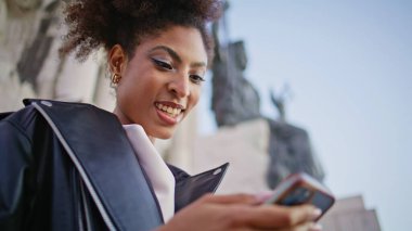 Cep telefonuna mesaj atan neşeli kız şehrin tarihi mimarisinin yanında duruyor. Gülümseyen Afrikalı Amerikalı kadın anıtın yanında akıllı telefon mesajları okuyor. Kıvırcık kadın cep telefonu uygulamasını dışarıda geziyor..