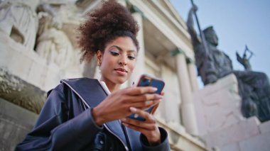 Gülümseyen bayan cep telefonu güzel antik mimarinin yanında duruyor. Kıvırcık Afrikalı Amerikalı kadın şehir heykelinin yanında cep telefonu mesajı okuyor. Mutlu esmer sohbet akıllı telefon.