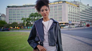 Pozitif esmer gezgin şehir hafta sonu alacakaranlık yakın çekim keyfini çıkarıyor. Gülümseyen Afro-Amerikan kadın modern caddede yürüyen kameraya bakıyor. Çekici kıvırcık kadın geceyi şehir meydanında yalnız geçiriyor..