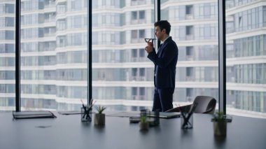 Profesyonel çalışan ofis panoramik penceresinin yanındaki akıllı telefondan sesli mesaj kaydediyor. Cep telefonu hoparlörüyle konuşan başarılı bir patron. Telefondaki ses bildirimini dikte eden kendinden emin iş adamı.