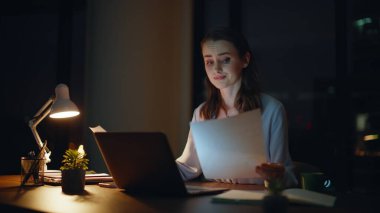 Gece iş yerindeki aşırı yüklenmiş çalışanlar belgeleri inceliyor. Endişeli iş kadını şirket raporlarını okuyor ve kendini yorgun hissediyor. Stresli kadın yönetici acı çeken şablonlara dokunuyor.