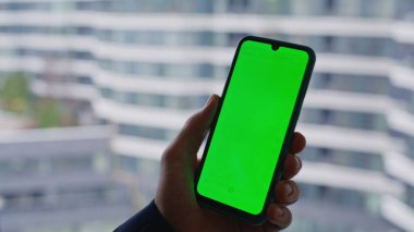 İş adamı, pencere kenarı manzaralı akıllı telefonu yakından takip ediyor. Tanımlanamayan yönetici yeşil ekran cep telefonu kullanarak internette sörf yapıyor. Girişimci tarama uygulaması kroma anahtar cep telefonu.