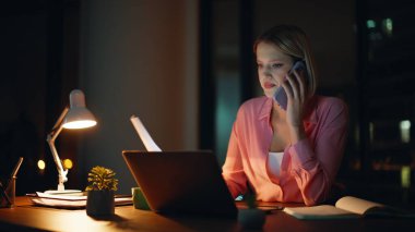 Uzaktan kumandalı profesyonel cep telefonuyla gece ofisinde mali dökümanları tartışıyor. Yorgun iş kadını akıllı telefondan fazla mesai yapıyor. Stresli kadın konuşuyor. Endişeli şirket raporu..