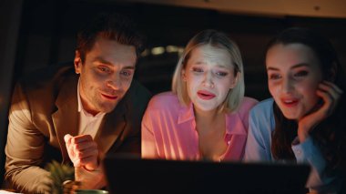 Kameralı bilgisayarda gülümseyen arkadaşlar gece evde yan yana oturuyorlar. Mutlu kadın adam dairede arkadaşça video görüşmesinden hoşlanıyor. Neşeli meslektaşlar gayri resmi atmosferde sanal buluşma.