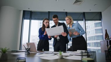 Grup arkadaşları modern konferans odasında proje belgelerini tartışıyorlar. Yaratıcı girişimde işbirliği yapan üç işletme yöneticisi. Grup çalışanları iş yerindeki belgeleri inceliyor..