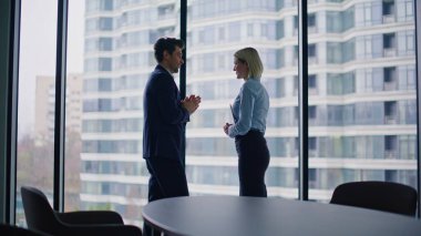 Ofis panoramik penceresinden şirket ortakları konuşuyor. Gülümseyen iş adamları şehir manzarası hakkında tartışıyorlar. İş kadını modern şirket işyerinde birlikte konuşuyor..