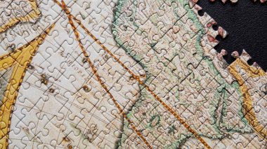 Tamamlanmamış dünya haritası bulmacası karanlık arka planda yatıyor ve yapıyı yakınlaştırıyor. Klasik zeka oyunu resmi. Tarihsel manzara ayrıntıları bir araya geliyor. Siyah üzerine toplanan yapboz