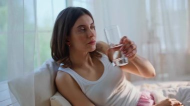 Erken yaşta su içen bir kadın rahat bir şekilde yatak örtüsüne oturur. Gülümseyen güzel bayan, uyanıp, yumuşak ev yatağında dinleniyor. Sakin esmer, sabahları bardaktan taze bir içecek yudumluyor..