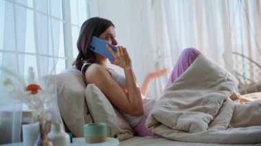 Rahat, esmer, konuşan cep telefonlu, rahat bir ev yatağı. Kaygısız kadın, aydınlık yatak odasında akıllı telefondan haberleri paylaşarak gülüyor. Gülümseyen bayan cep telefonunu arıyor. Rahat bir yatakta dinleniyor..