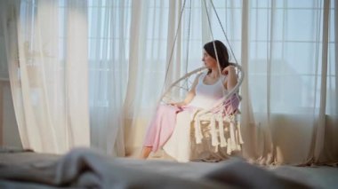 Huzurlu kadın yatak odasının içinde sallanan sandalyede sallanıyor. Kaygısız esmer, halat koltukta dinleniyor ve hafta sonunun tadını çıkarıyor. Mutlu pijama giymiş kadın bacaklarını açıyor ve rahatlıyor..