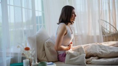 Bayan evinde rahat bir şekilde yatarken acı çeken bir dönem geçiriyor. Sabahın erken saatlerinde karın ağrısı çeken üzgün bir kadın karnına dokunuyor. Mutsuz esmer, apartman yatağında karın krampları yaşıyor..