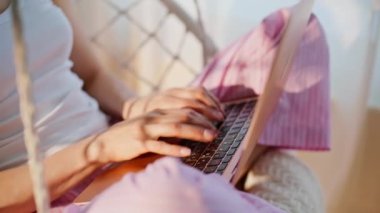Pijamalı kız rahat bir sandalyede oturmuş dizüstü bilgisayarı daktilo ediyor. Kadın, sabah dairesinde bilgisayarın tuşlarına basarak e-posta yazıyor. Çevrimiçi internet sitesinde çalışan gevşemiş serbest kadın..