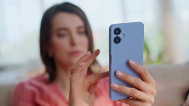 Oturma odasındaki kanepeye yakın oturan bayan cep telefonu uygulaması. Güzel bir kadın akıllı telefonları daire kanepesinde çevrimiçi mesaj okuyarak kaydırıyor. E-ticaret mağazasında telefon kullanarak rahatlamış esmer alışverişi..