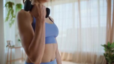 Hafif apartman iç kısmında dambıl egzersizi yapan genç bir sporcu. Spor kadını ağırlık kaldırıyor. Sabah evde egzersiz yaparken kaslarını çalıştırıyor. Formda sporcu kadın halter çalışıyor..