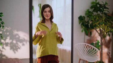 Kendine güvenen bir kadın aynada gömleğini ayarlıyor ve görünüşünü tatmin ediyor. Şık bir bayan gün ışığında kıyafet hazırlıyor. Gülümseyen esmer yansımaya hayran evde şık kıyafetlerin tadını çıkarıyor..