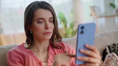 İnternetten akıllı telefon almayı seçen bir kadın daire kanepesinde yakın plan çekiyor. İnternet alışverişinden keyif alan gülümseyen bir kadın cep telefonu uygulaması kullanıyor. Cep telefonuyla sipariş veren mutlu müşteriler.
