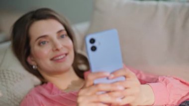 Rahat bir bayan cep telefonuna mesaj atıp rahat bir kanepede yatıyor. Gülümseyen esmer, mesajlaşan akıllı telefon rahat bir kanepede dinleniyor. Kaygısız kadın sosyal medyada telefonla sohbet etmekten zevk alıyor.