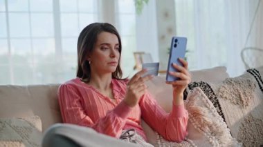 Akıllı telefon ödemesi yapan bir kız kredi kartı bilgilerini internet uygulamasına yüklüyor. Gülümseyen kadın alışverişçi internet e-ticaret alışverişinin keyfini çıkarıyor. Mutlu esmer, telefonla mal sipariş ediyor..