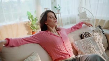 Modern oturma odasındaki koltuğa düşen gülümseyen kadın. Yakın plan. Rahatlamış genç bayan rahat bir kanepede otur ve hafta sonu tatilinin tadını çıkar. Kaygısız esmer, evinde dinleniyor..