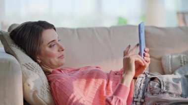 Ev kızı cep telefonuyla sosyal medyayı izliyor rahat kanepe kapanışı yapıyor. Gülümseyen genç kadın rahat koltukta dinlenen haber yayını yapıyor. Dairedeki cep telefonunda gezinen mutlu bayan.