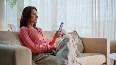 Mutlu bir kadın cep telefonuna bakıyor rahat bir kanepe kapanışı yapıyor. Gülümseyen esmer daire kanepesindeki cep telefonu uygulamasını kullanarak internetten sipariş veriyor. Evde akıllı telefon mesajı okuyan rahat bir bayan..